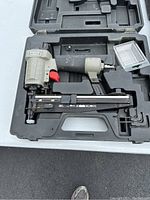 Porter-Cable finish nailer with red trigger and short magazine, stored in a molded black plastic case with nails and accessories