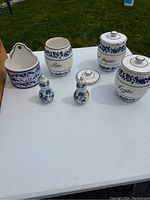 Full set of antique German porcelain kitchen containers and shakers with blue floral pattern on a white background, displayed on a white table outdoors.