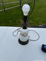 Full view of porcelain lamp base with floral hand-painted design and metal base, cord visible, no shade.