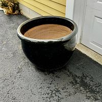 Black glazed terracotta pot placed on asphalt near a building wall.
