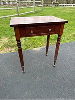 Full view of the wooden sewing table with turned legs and drawer, showing wear and need for refinishing.