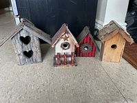 Four decorative birdhouses on a floor showing general condition and style.