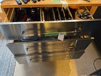 Three stainless steel kitchen drawers partially open showing organizer trays filled with cutlery and utensils.