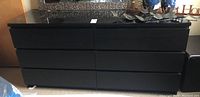 Full view of black six drawer dresser with glass top and no visible handles.