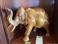 Frontal side view of wooden elephant sculpture showing whole body, legs, trunk, and tusks.