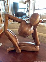 Front view of the wooden abstract figure sculpture on a table with living room background visible.