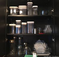 Full view of shelves with plastic containers and glass canisters, including Pyrex mixing bowl on top right shelf