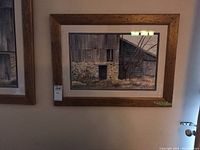 View of one framed print showing a barn with stone foundation and wooden siding, hung on a wall.
