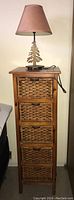 Full view of the wood storage unit with five wicker drawers topped with the table lamp.