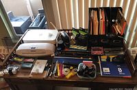 Desk with office supplies including HP printer, Fellowes laminator, organizers with folders, writing tools, clips, tape, and stamp.