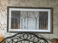 Full view of the framed print artwork featuring stylized trees with bare branches in muted earth tones, hung on wallpapered wall.