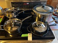 Photo showing three Cuisinart stainless steel pots with lids of varying sizes, a large stainless steel pot with glass lid, and a cast iron frying pan on stovetop.