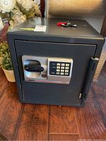 Front and angled view of black Sentry safe featuring electronic keypad lock panel, handle, and hinge. Some surface scratches and wear.