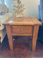 Front view of solid wood side table with drawer and decorative coral piece on top.