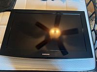 Front view of Samsung television with black bezel displaying reflection of ceiling fan.
