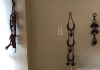 Photo shows one pair of large and one narrower vintage wooden and metal ice skates hanging on a wall next to two decorative sets of rustic metal cow bells.