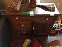 Front view of the wooden washstand showing three drawers in the center and cabinet doors on each side with white round knobs.