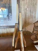 Pair of triangular wooden candle holders each holding a taper candle, shown on a wooden surface against a wood-paneled background.
