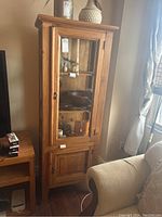 Front view of tall wooden display case with glass door and decorative items inside.