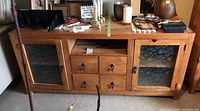Front view of the rough wood TV stand showing two textured glass doors, four drawers, and open cubby space with items on top.