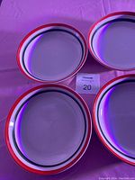 Four ceramic soup plates arranged to show the flat surface and rim color pattern of red, blue, and black concentric stripes.