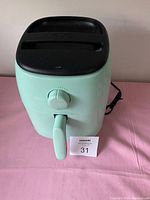 Front view of the Dash compact air fryer showing light green color, black top with vent slots, single dial and pull handle.