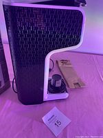 Side view of the black and white coffee maker showing textured patterned side panel and paper bag item next to it.