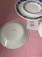 Corelle plate with blue floral pattern on edge and Corelle brand mark on bottom, displayed on pink tablecloth.