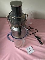 Electric juicer with metallic and transparent plastic parts including wide feed chute, clear pitchers with handles, and power cord.