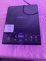 Top view of black Living Basics hotplate with circular heating area, digital control panel on front edge showing power and function buttons.