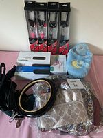 Photo of assorted items including four selfie sticks in boxes, a Bluetooth speaker box, blue fuzzy slippers with moon embroidery, a beige patterned pouch, and multiple bags on a pink surface.