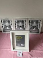 Four picture frames on a pink surface. Three frames are identical white marble-effect with black and white placeholder image. One smaller white wooden frame stands in front.