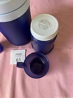 Photo showing small blue insulated thermos with white lid and matching blue plastic cup with handle