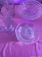 Photo showing six tall clear drinking glasses and various sized etched floral patterned glass bowls and plates.