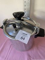 Top view of aluminum pressure cooker with sealed lid and black plastic top handle featuring a pressure release valve, next to a ruler for size comparison.