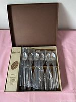 Open original box showing six long drink spoons with twisted handles, some wrapped in plastic.