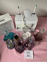 Overview of electric toothbrush holder with two toothbrushes, facial steamer box, assorted bottles, cotton rounds, and cosmetic items on pink surface
