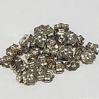 Pile of multiple small 10K white gold earring backs shaped like flowers.