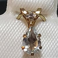 Front view of pendant showing pear-shaped aquamarine and round clear stone in 10K yellow gold setting.