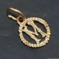 Close-up photo of a small circular pendant in yellow gold with the letter 'M' cut out in the center and a scalloped edge. Includes the bail for chain attachment.