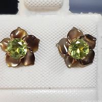 Pair of 10K yellow gold earrings with peridot in a flower design, each earring featuring a faceted round peridot center and detailed petals with a brownish tone.