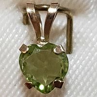 Close-up front view of the heart-shaped peridot pendant in 10K yellow gold on white fabric.