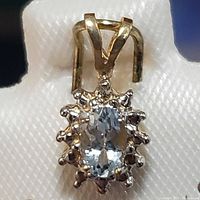 Close-up front view of the 14K yellow gold pendant with an oval aquamarine gemstone surrounded by small round diamonds in cluster setting.