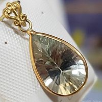 Close-up front view of a pear-shaped green amethyst pendant set in 14K yellow gold with ornate bail.