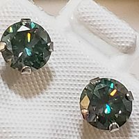 Close-up image of two round cut moissanite stones set in 14K white gold prong studs against textured white background.