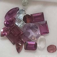 Photo showing a variety of genuine faceted gemstones in different colors and cuts arranged on a white surface