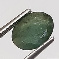 Close-up image showing an oval cut green emerald held by tweezers with visible inclusions and cracks.