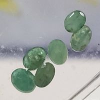 Seven oval-shaped green gemstones identified as genuine emeralds, displayed on clear surface.
