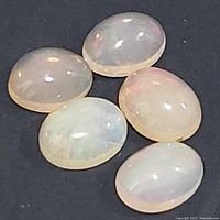 Five oval genuine opal cabochons arranged on black background showing their smooth polished surface and flashes of iridescent color.
