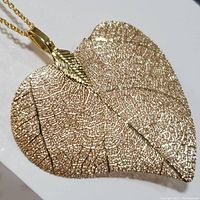 Close-up photo showing the gold-colored natural leaf pendant with detailed textured veins on a link chain.